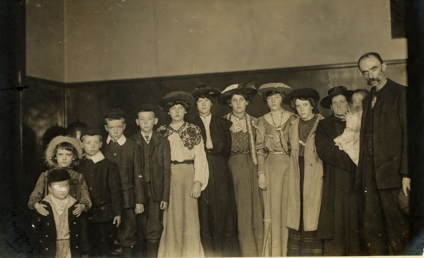A large Scottish family of parents and children stands in a row for a portrait at Ellis Island